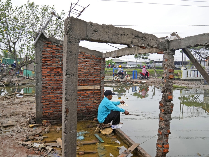 A man fishes in water inundating the area around an abandoned building due the rising sea levels and land subsidence in Sidogemah, Central Java, Indonesia